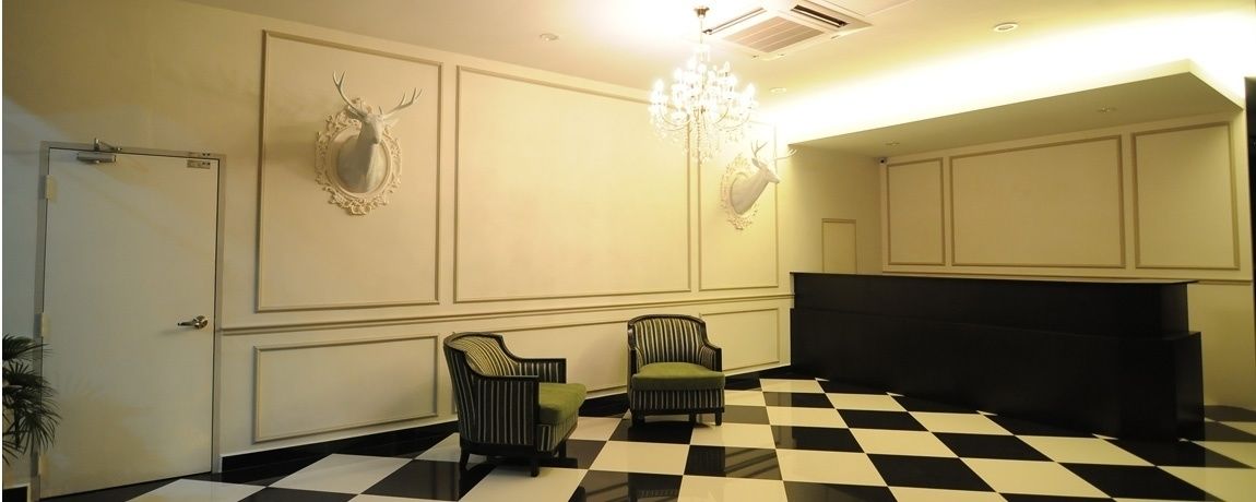 A lobby with a checkered floor, two armchairs, a chandelier, and a wall-mounted deer head decoration.