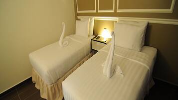 Quarto de hotel com duas camas, cada uma com colcha e travesseiros brancos, e uma mesinha de cabeceira com abajur entre elas.