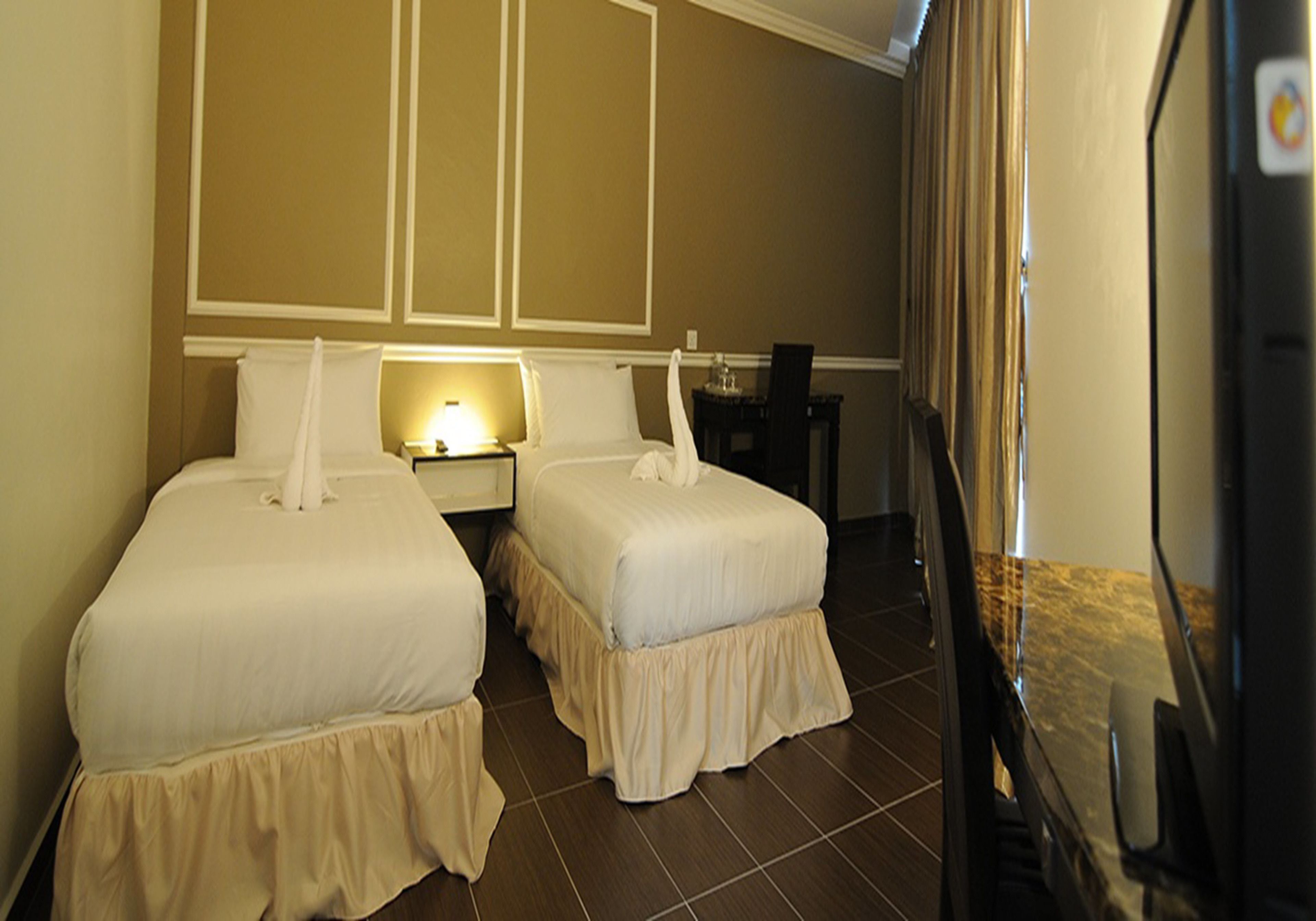 A hotel room with two beds, a nightstand, a lamp, and a desk with a chair.