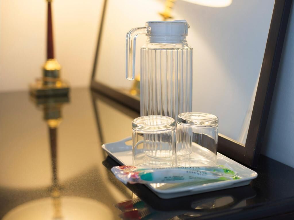 A clear glass bottle with a pump, two small glasses, and a packet of snacks on a tray.