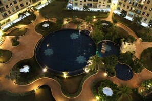 An aerial view of a hotel courtyard with multiple pools, palm trees, and well-lit pathways. - Putra Place Home Inn (George Town)