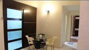 A dining area with a glass table and chairs, a dark door with frosted glass panels, and a wall-mounted light fixture. - Putra Place Home Inn (George Town)