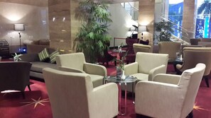 A hotel lobby with a sofa, armchairs, a coffee table, a large potted plant, and a staircase. - Galaxy Hotel Banjarmasin (Banjarmasin)
