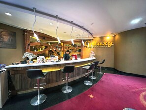 A bar area with a Galaxy-themed sign, a bartender, and a counter with stools. - Galaxy Hotel Banjarmasin (Banjarmasin)