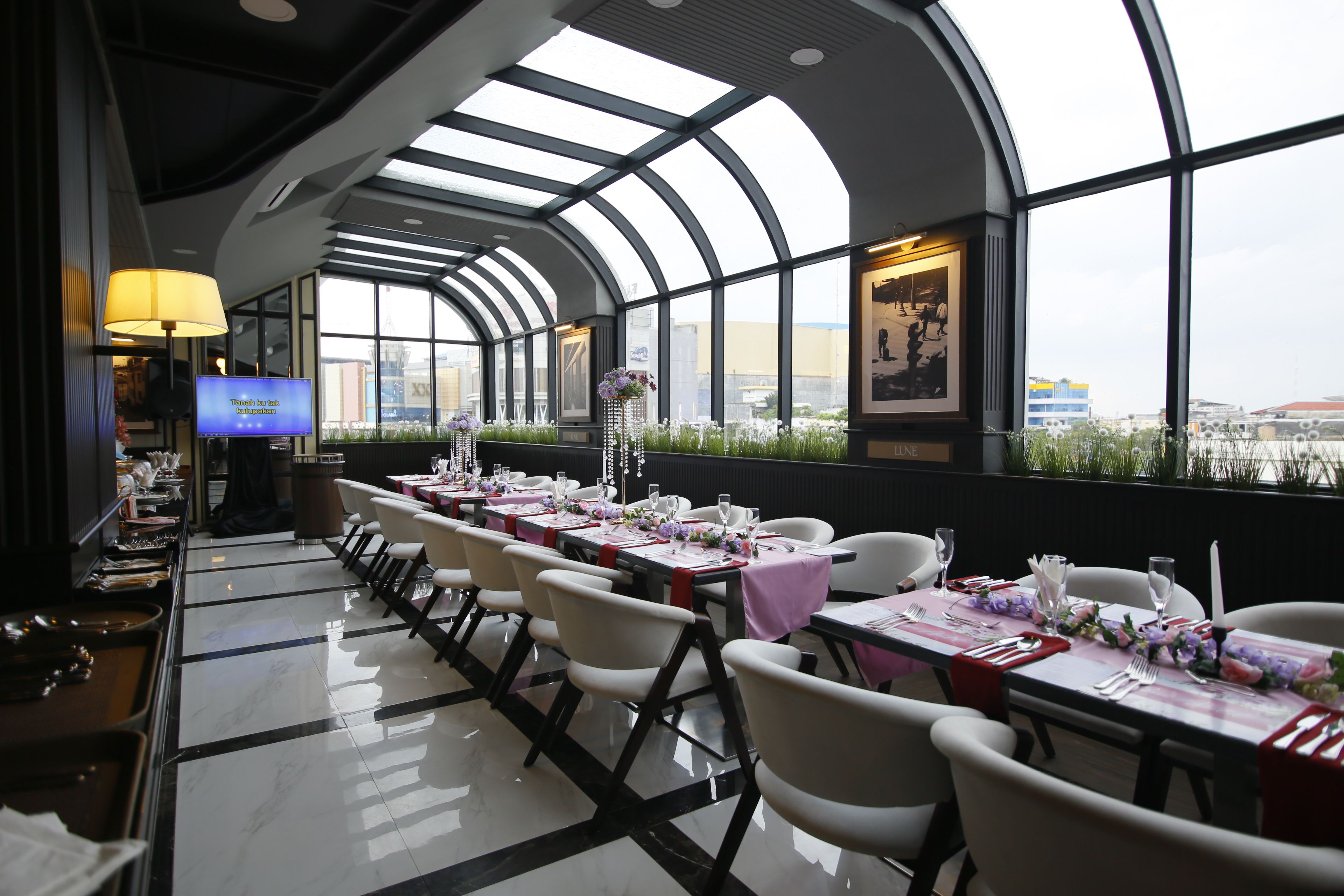 A restaurant with a long table layout, a TV screen, and framed artwork on the walls.