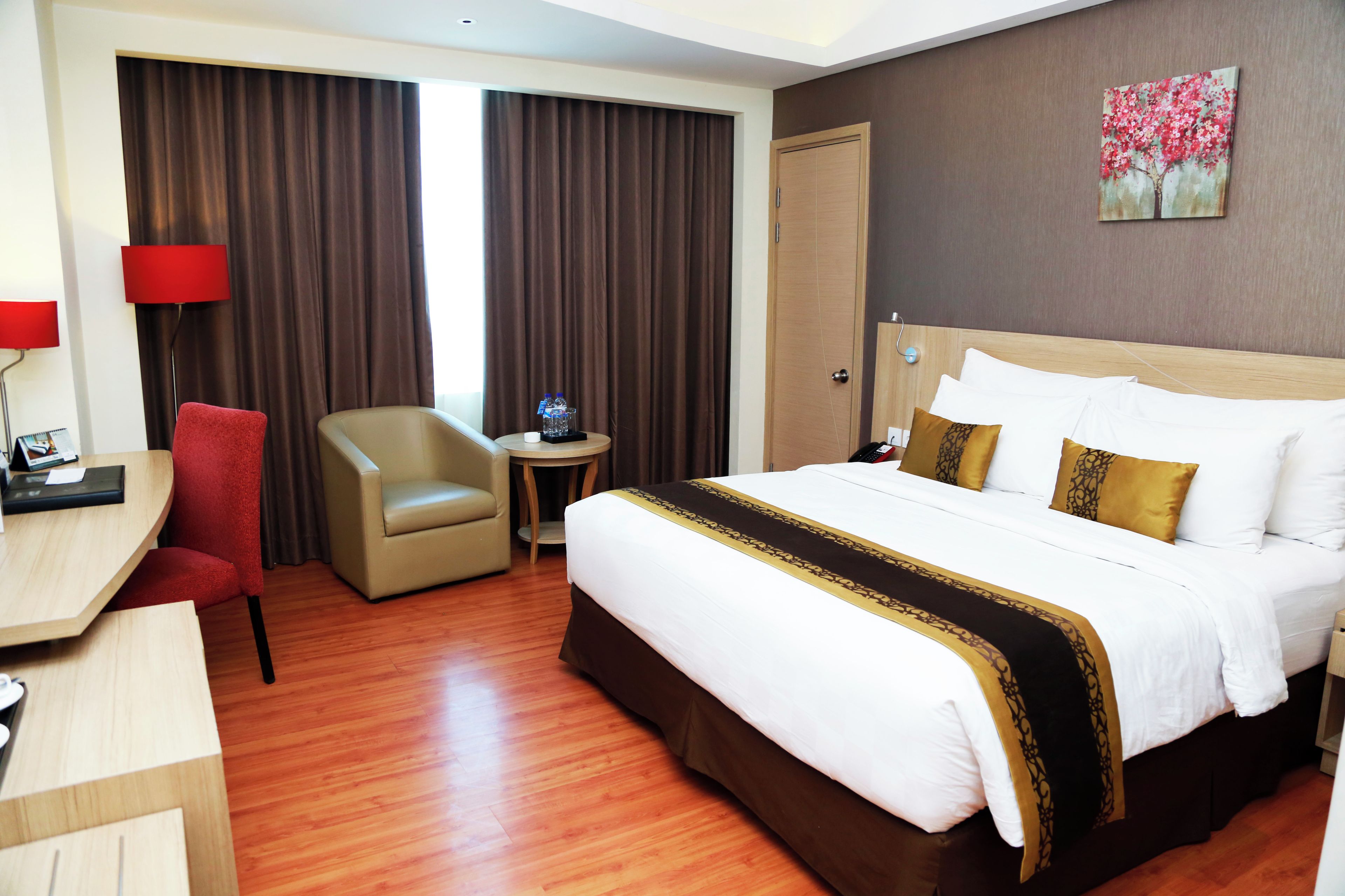 A hotel room with a bed, a desk, a chair, a round table, and a painting on the wall.