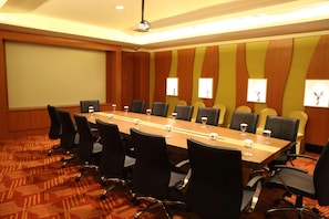 A conference room with a long table, black chairs, and a projector screen. - Galaxy Hotel Banjarmasin (Banjarmasin)