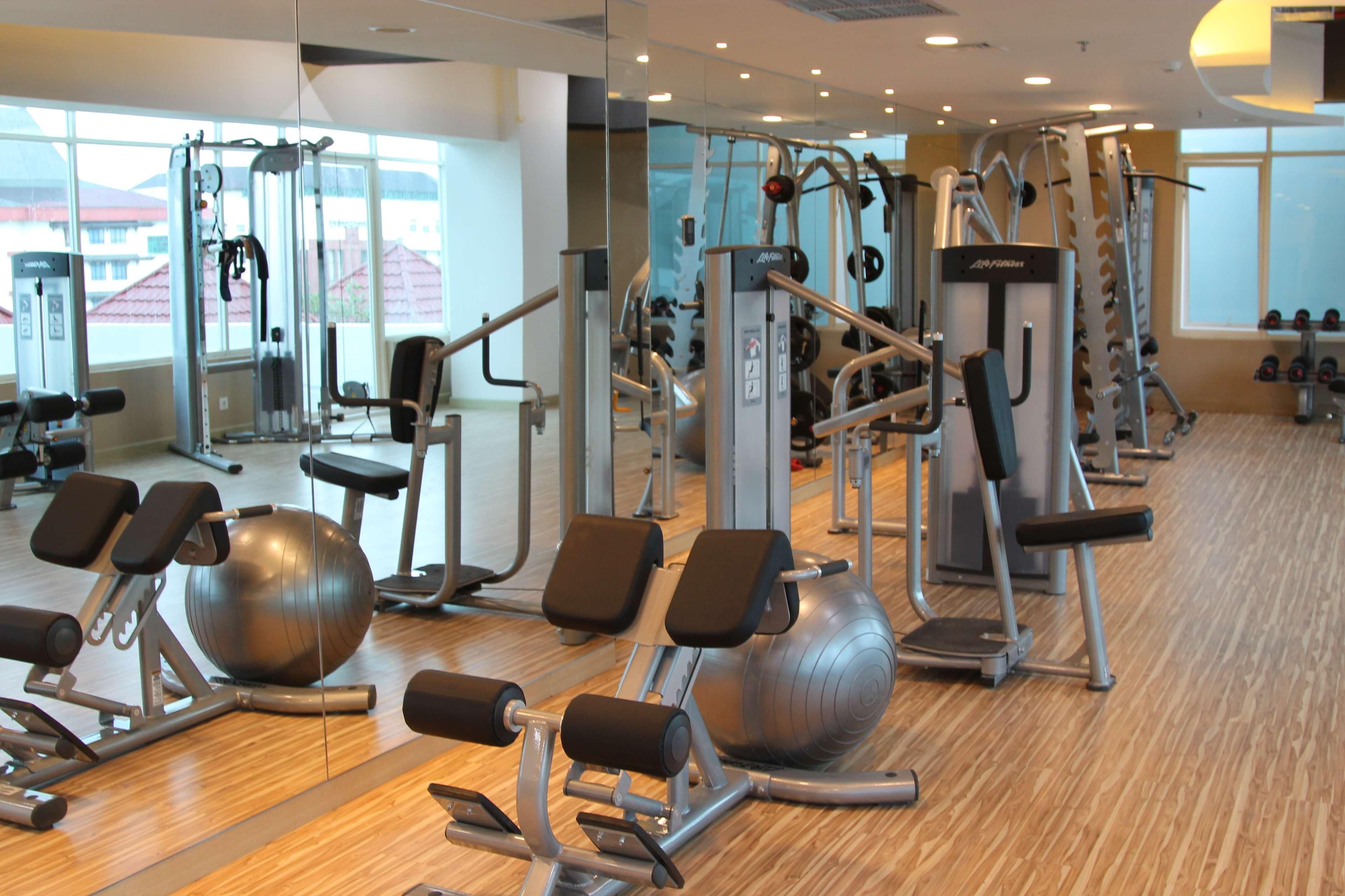 A gym with various exercise equipment, large windows, and a wooden floor.