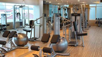 A gym with various exercise equipment, large windows, and a wooden floor.