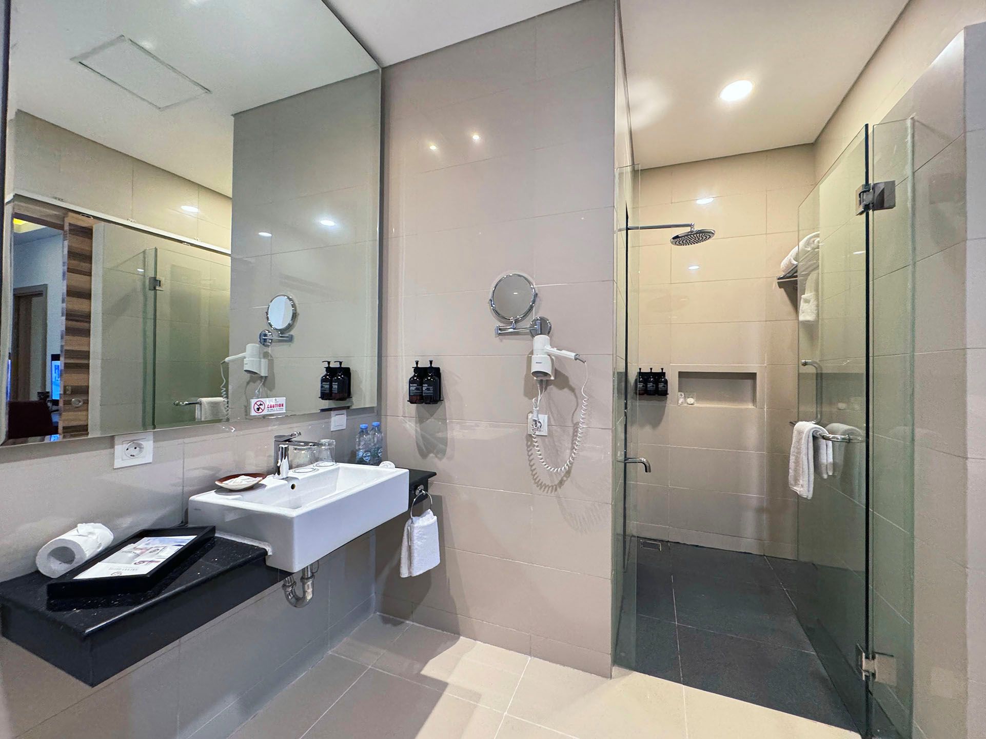 A modern bathroom with a glass shower enclosure, a large mirror, and a vanity with a sink and towel rack.