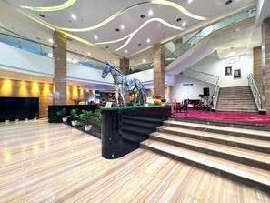 A modern hotel lobby with a central staircase, a Galaxy-branded wall, and a large horse sculpture. - Galaxy Hotel Banjarmasin (Banjarmasin)
