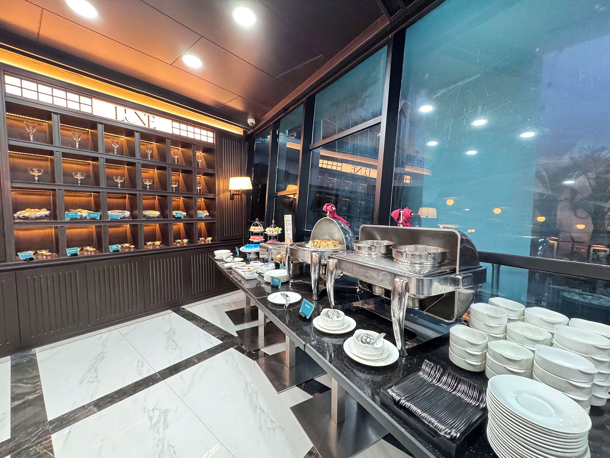 A buffet setup with a variety of dishes, a wine display, and a view of the city through large windows.