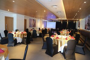 Un salón de conferencias con varias mesas, sillas negras y una pantalla grande.