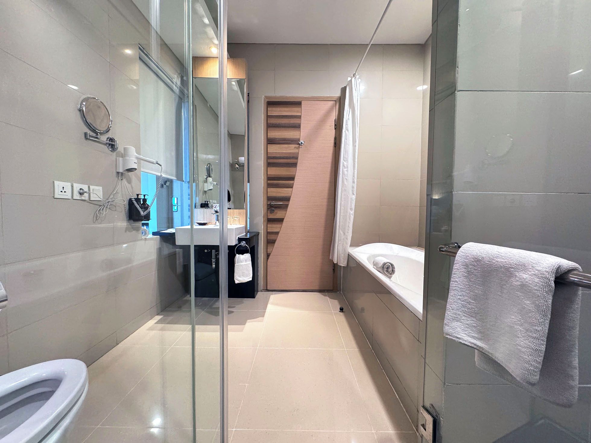 A modern bathroom with a glass shower enclosure, a toilet, a sink with a mirror, and a bathtub with a towel.