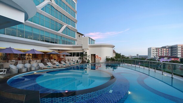 Un hôtel moderne doté d’une grande piscine intérieure, de chaises longues et offrant une vue sur le panorama urbain.