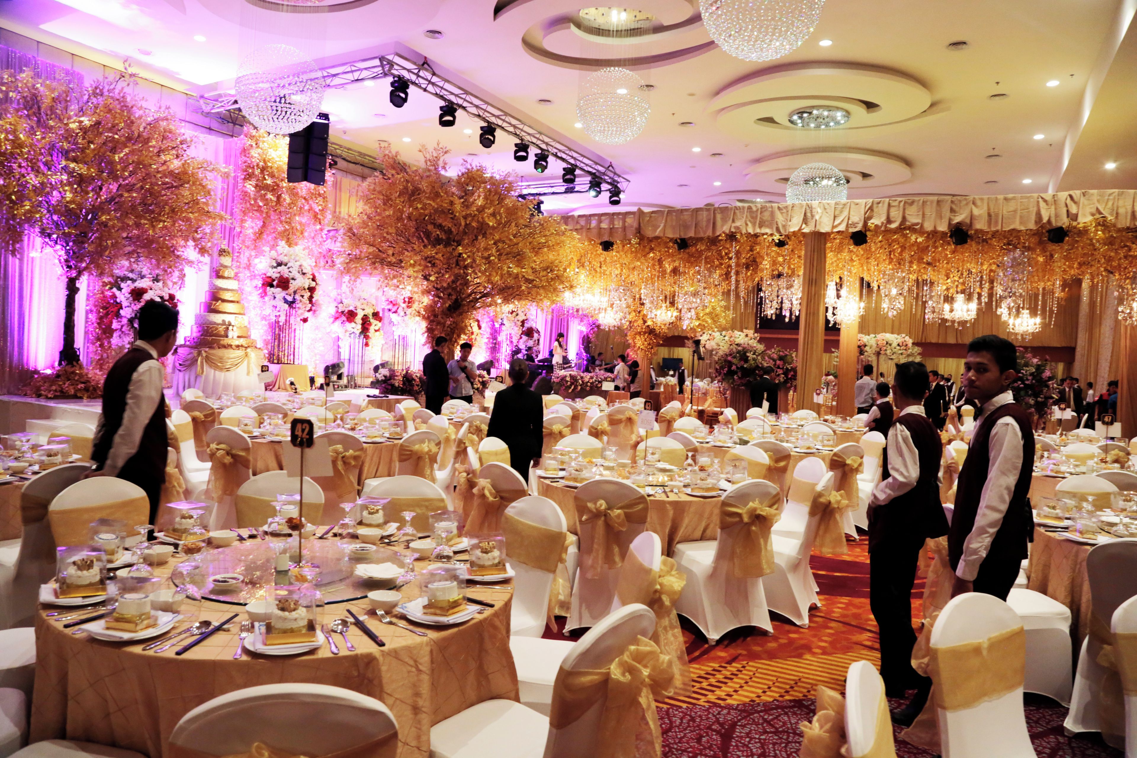A banquet hall with round tables, white chairs, and a stage with floral decorations.