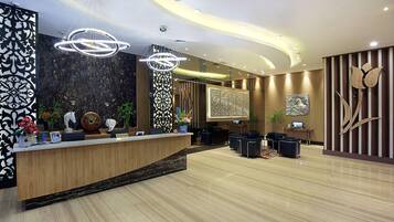 A modern reception area with a wooden reception desk, two large chandeliers, and a large wall-mounted artwork.