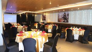 Un salón de conferencias con varias mesas dispuestas para comer, un escenario y una pantalla grande.