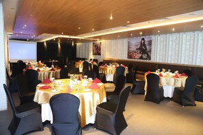 A conference room with multiple tables set for dining, a stage, and a large screen. - Galaxy Hotel Banjarmasin (Banjarmasin)