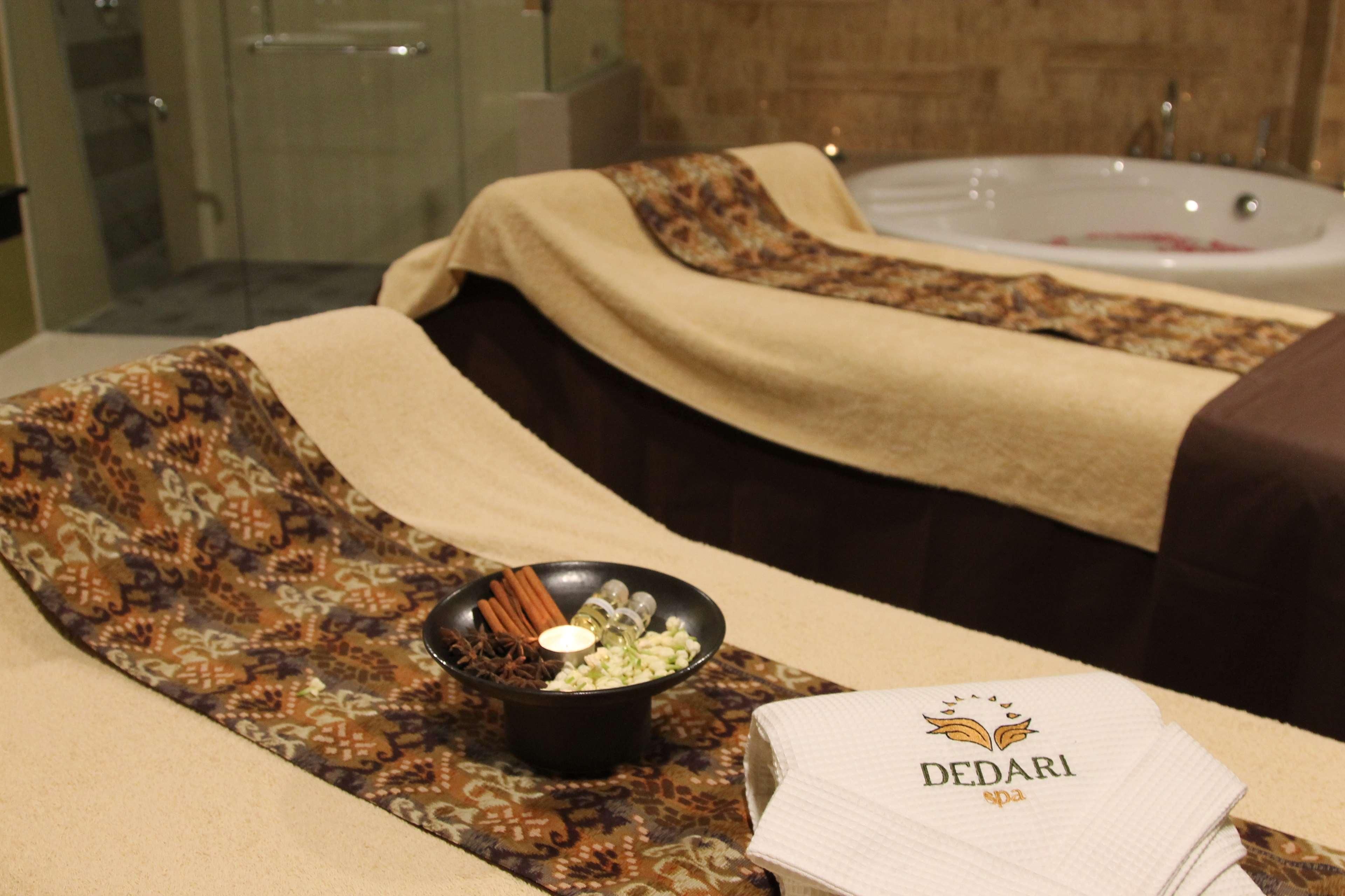 A spa room with a massage table, a bowl of essential oils, and a stack of towels with the spa's logo.