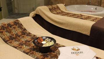 A spa room with a massage table, a bowl of essential oils, and a stack of towels with the spa's logo.