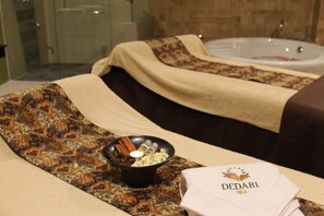 A spa room with a massage table, a bowl of essential oils, and a stack of towels with the spa's logo. - Galaxy Hotel Banjarmasin (Banjarmasin)
