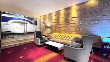 A modern lounge with a sofa, armchairs, a coffee table, a glass wall with a smoking area, and a wooden wall with recessed lighting.