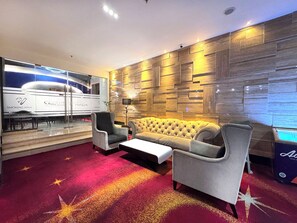 A modern lounge with a sofa, armchairs, a coffee table, a glass wall with a smoking area, and a wooden wall with recessed lighting. - Galaxy Hotel Banjarmasin (Banjarmasin)