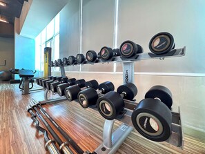 Un gimnasio con equipo de levantamiento de pesas, incluyendo mancuernas y barras, organizadas en estantes y bancos.