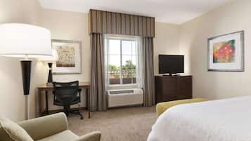 Een hotelkamer met een bed, een bureau met stoel, een televisie en een raam met gordijnen.