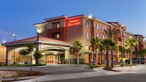 Un hotel Hampton Inn & Suites con fachada moderna, varios pisos y un área de entrada bien cuidada con palmeras y un paseo techado.