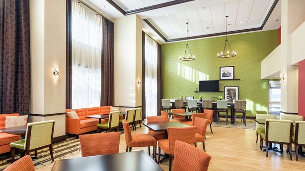 Vestíbulo de hotel con asientos naranjas, una pared de acento verde y un televisor de pantalla plana montado sobre un mostrador de recepción.
