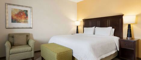 A hotel room with a large bed, two bedside lamps, a chair, and a small table.