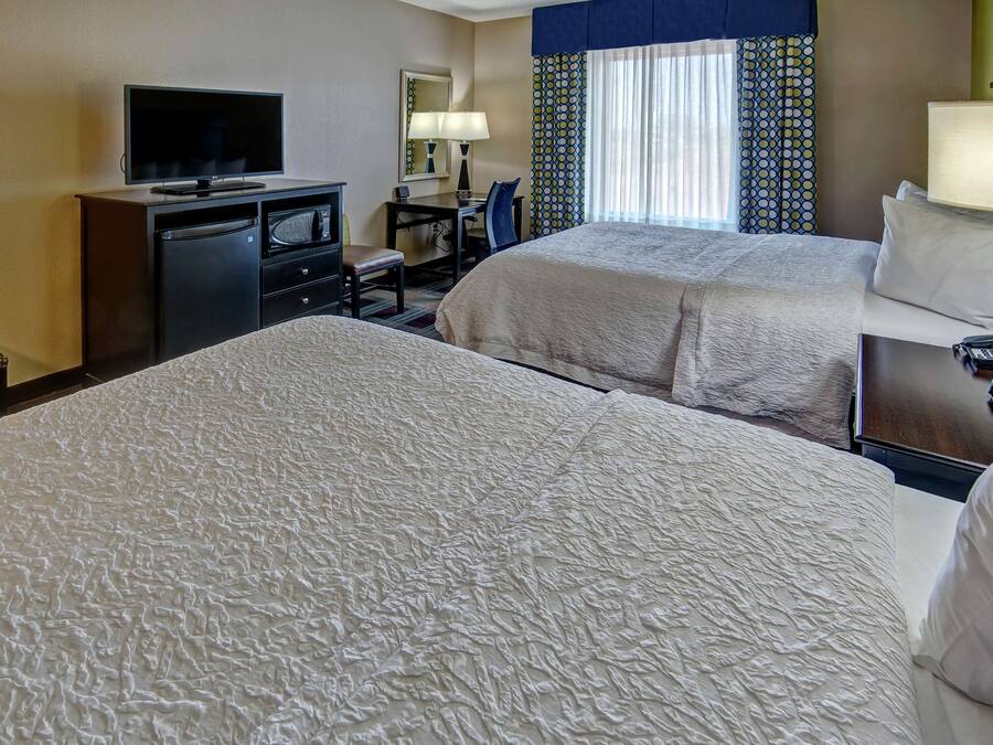 A hotel room with two beds, a desk with a chair, a television, and a desk lamp.