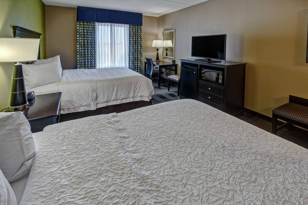 A hotel room with two beds, a desk with a computer, a television, and a desk lamp.
