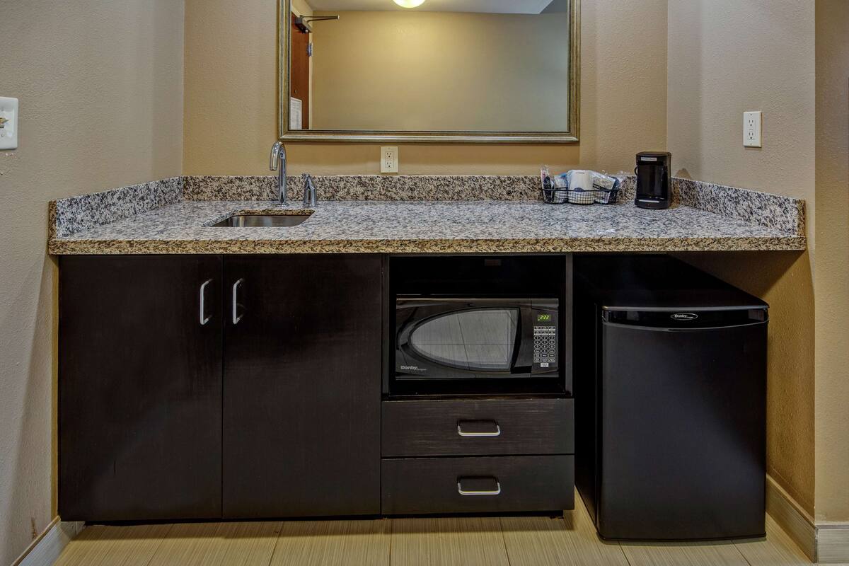 A compact kitchen with a granite countertop, a built-in microwave, a coffee maker, and a refrigerator.