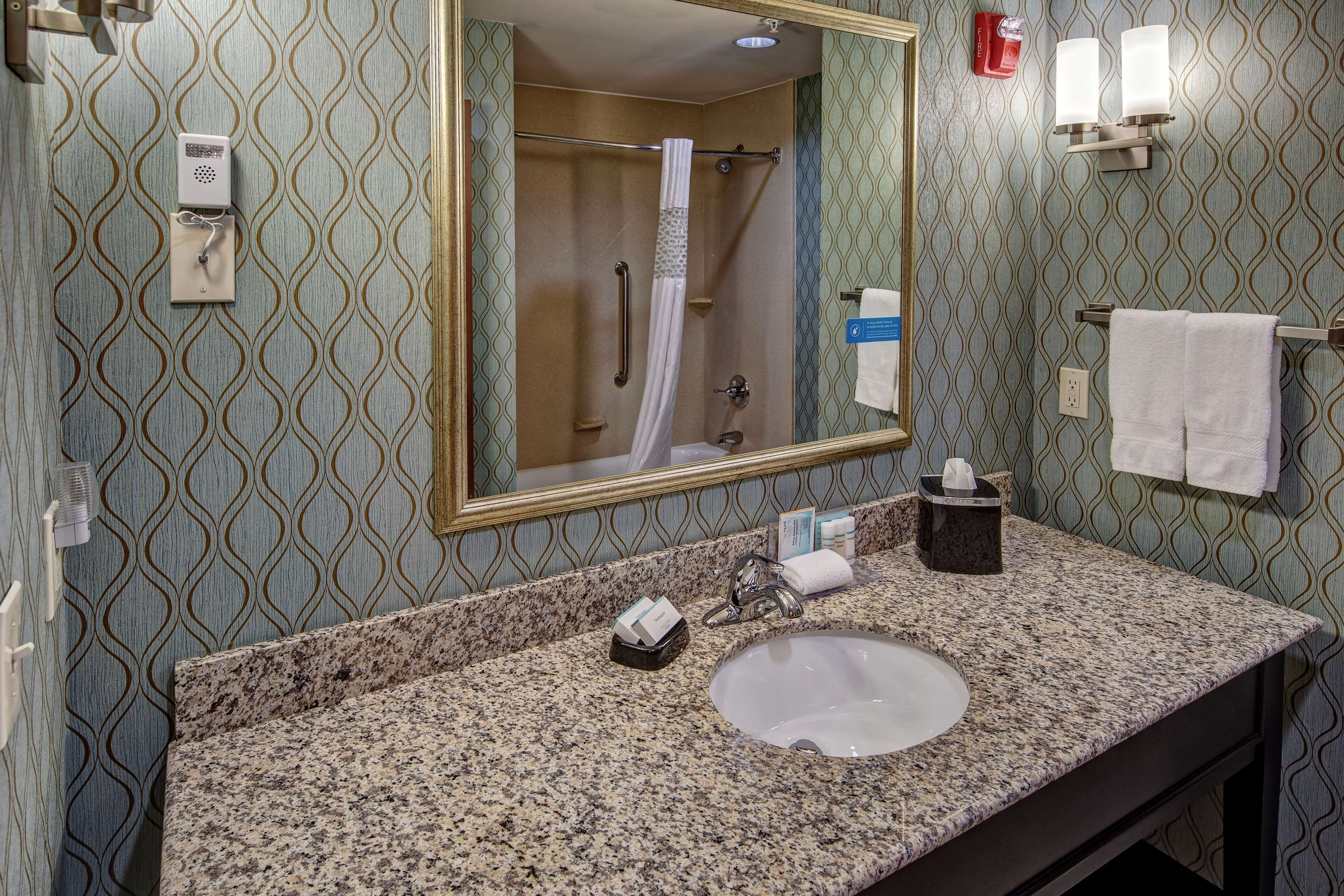 Une salle de bain avec un comptoir en granit, un lavabo, un miroir, un porte-serviettes et une douche avec un rideau.