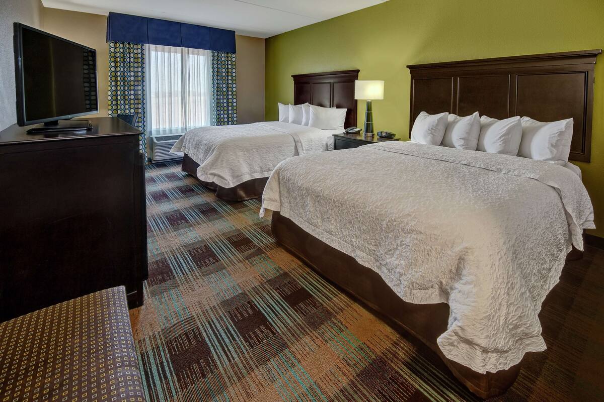 A hotel room with two beds, a TV, a desk, and a patterned carpet.