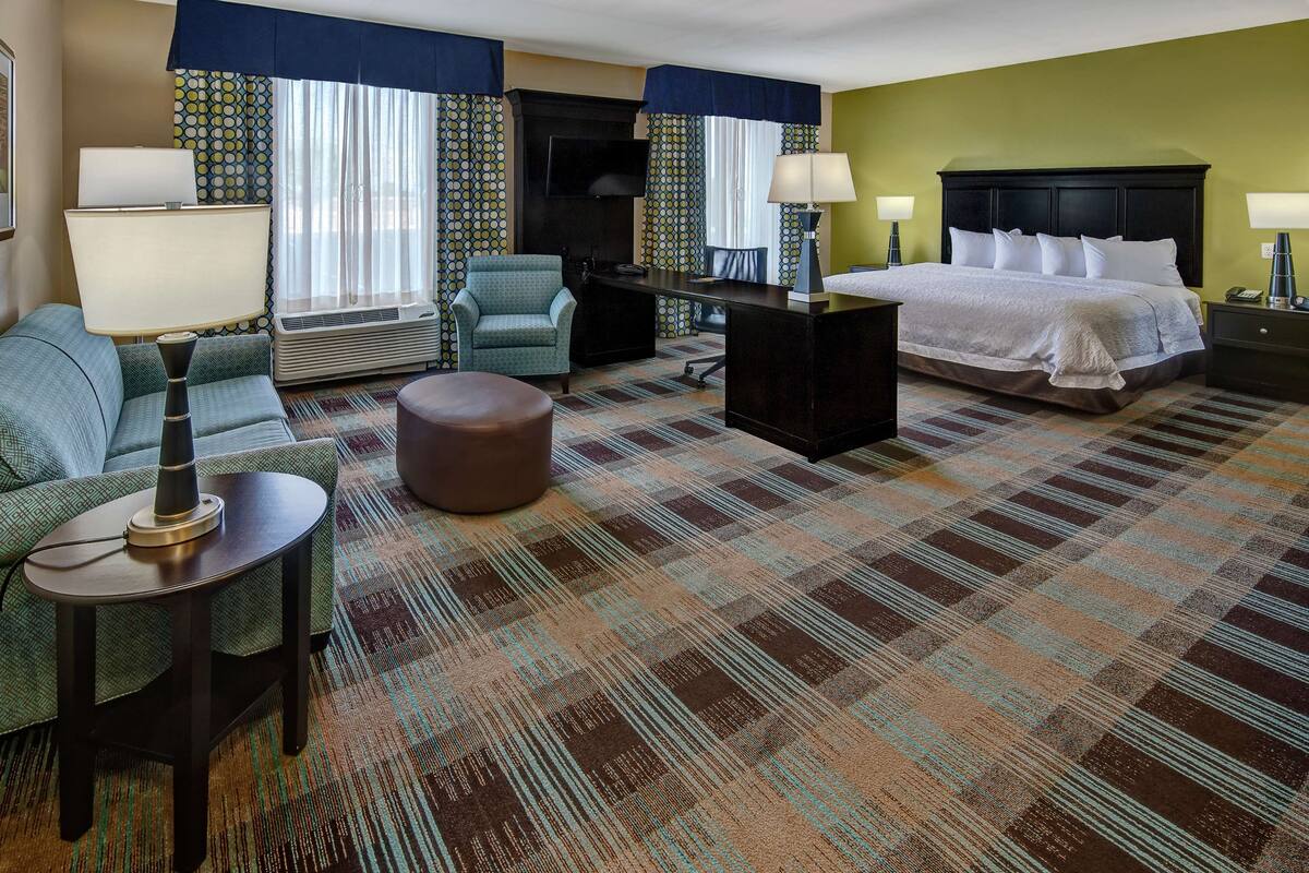 A hotel room with a bed, a desk, a chair, a sofa, and a television.