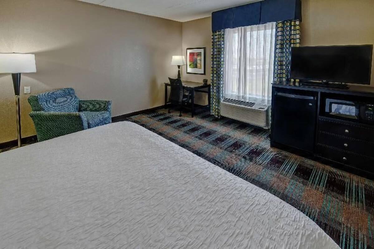 A hotel room with a large bed, a desk with a chair, a television, and a patterned carpet.
