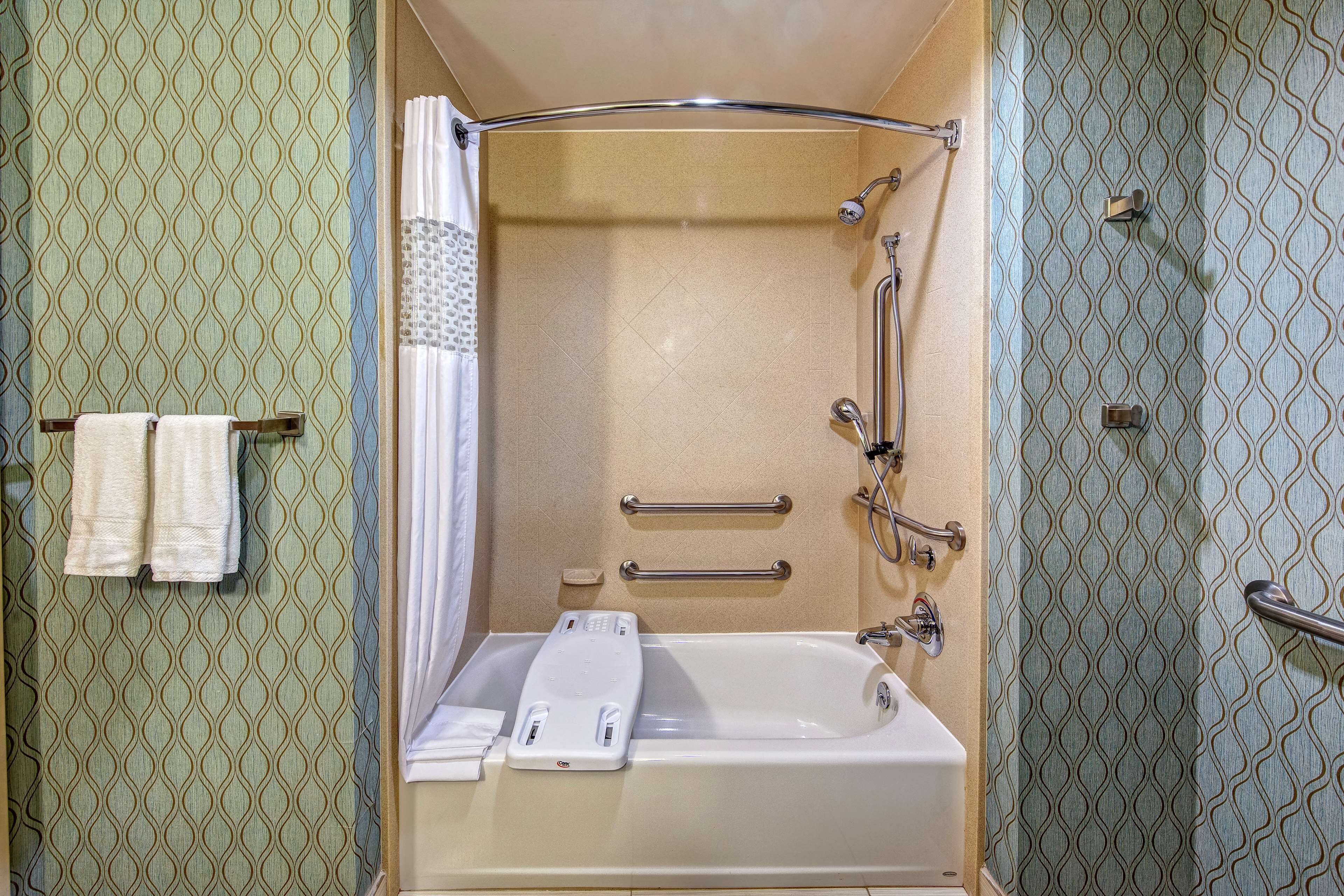A bathroom with a bathtub, a shower, and a toilet. There are two handrails and a towel rack with towels.
