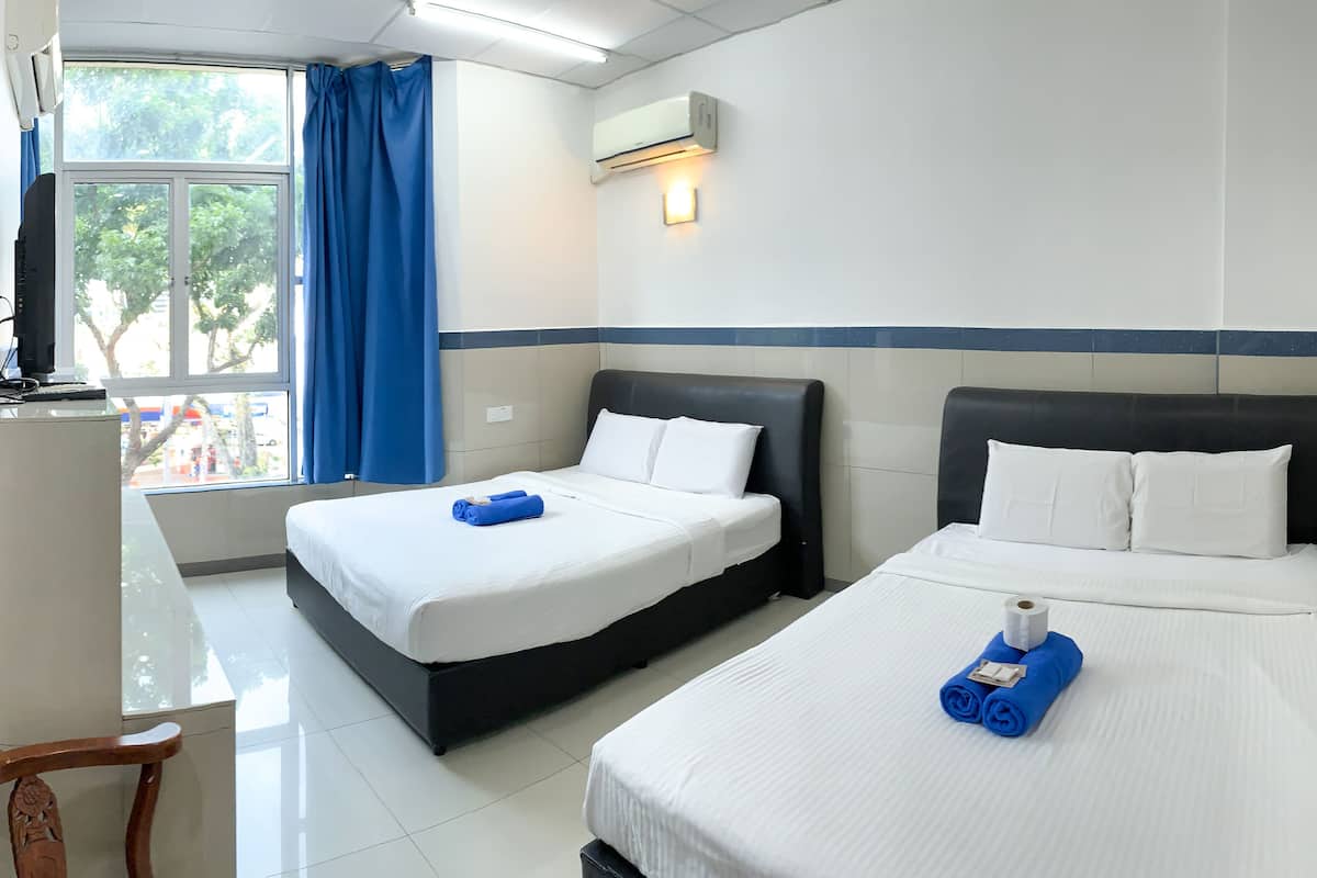 A hotel room with two beds, a desk, and a window with blue curtains.