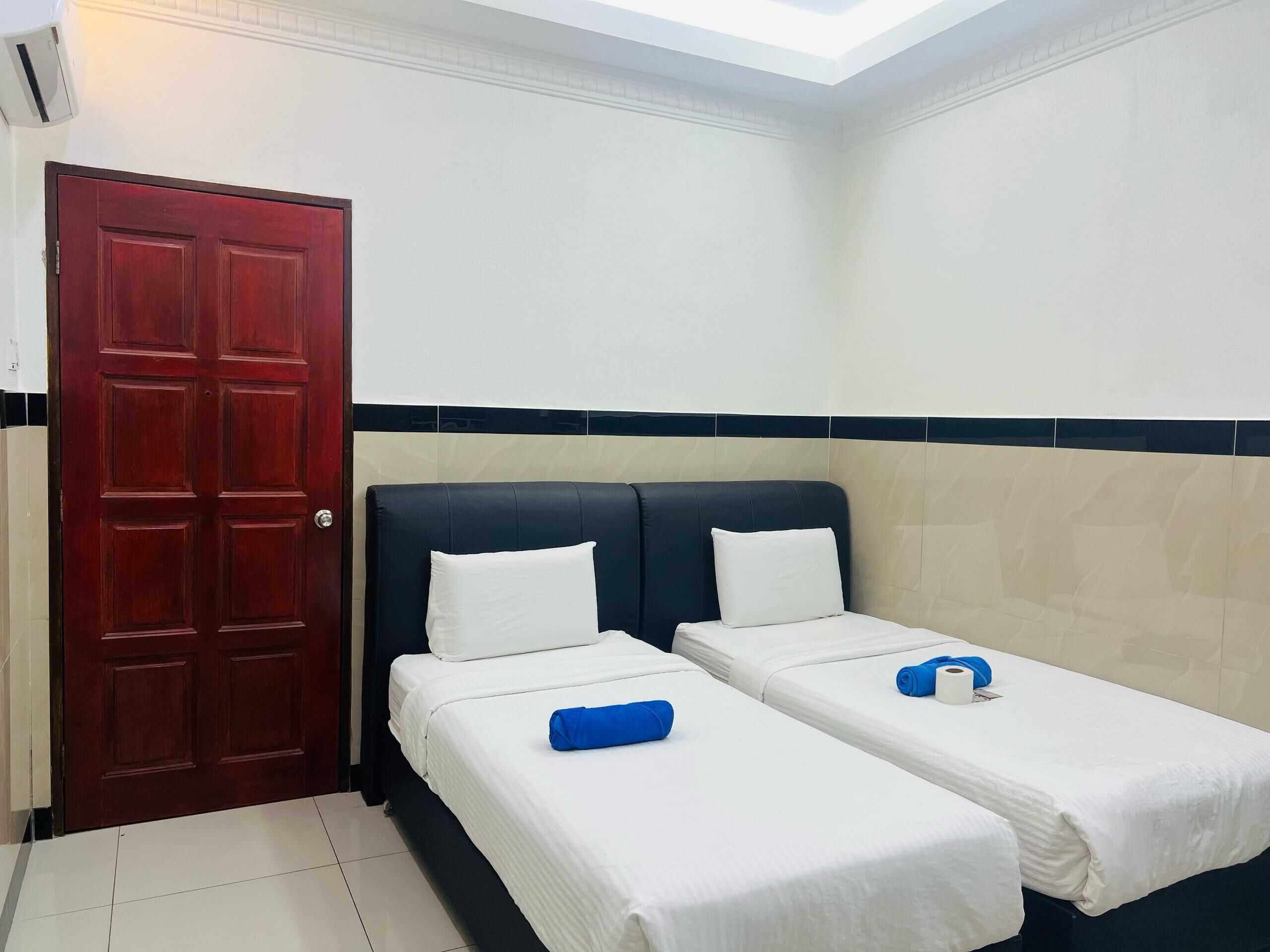Una habitación de hotel con dos camas individuales, una puerta roja y un tragaluz.