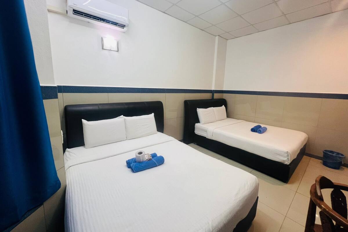 A hotel room with two beds, a blue curtain, an air conditioning unit, and a small wooden chair.