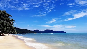 Une plage avec un ciel dégagé, une eau calme et des montagnes à l’horizon.