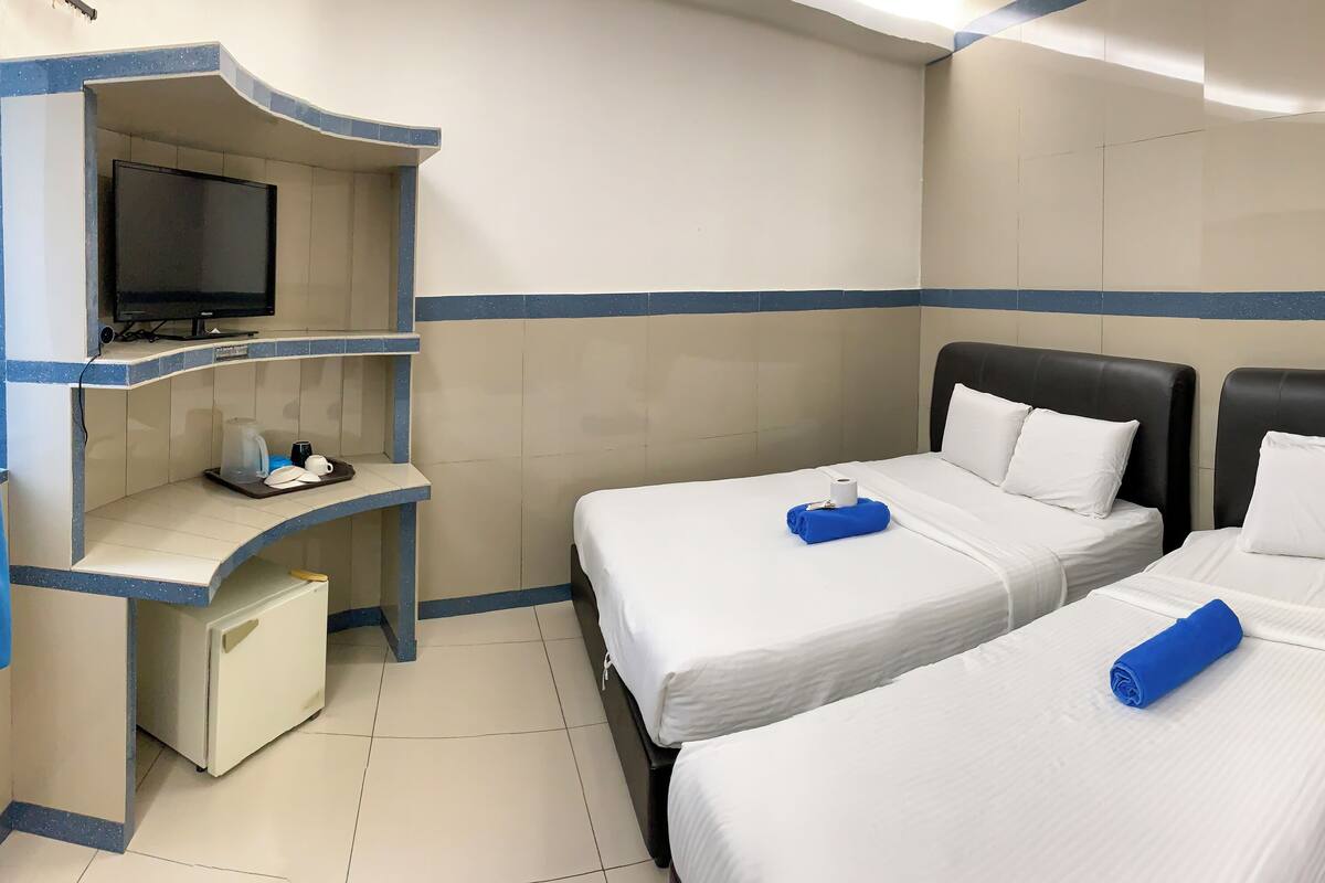 A hotel room with two beds, a desk with a television, and a small refrigerator.