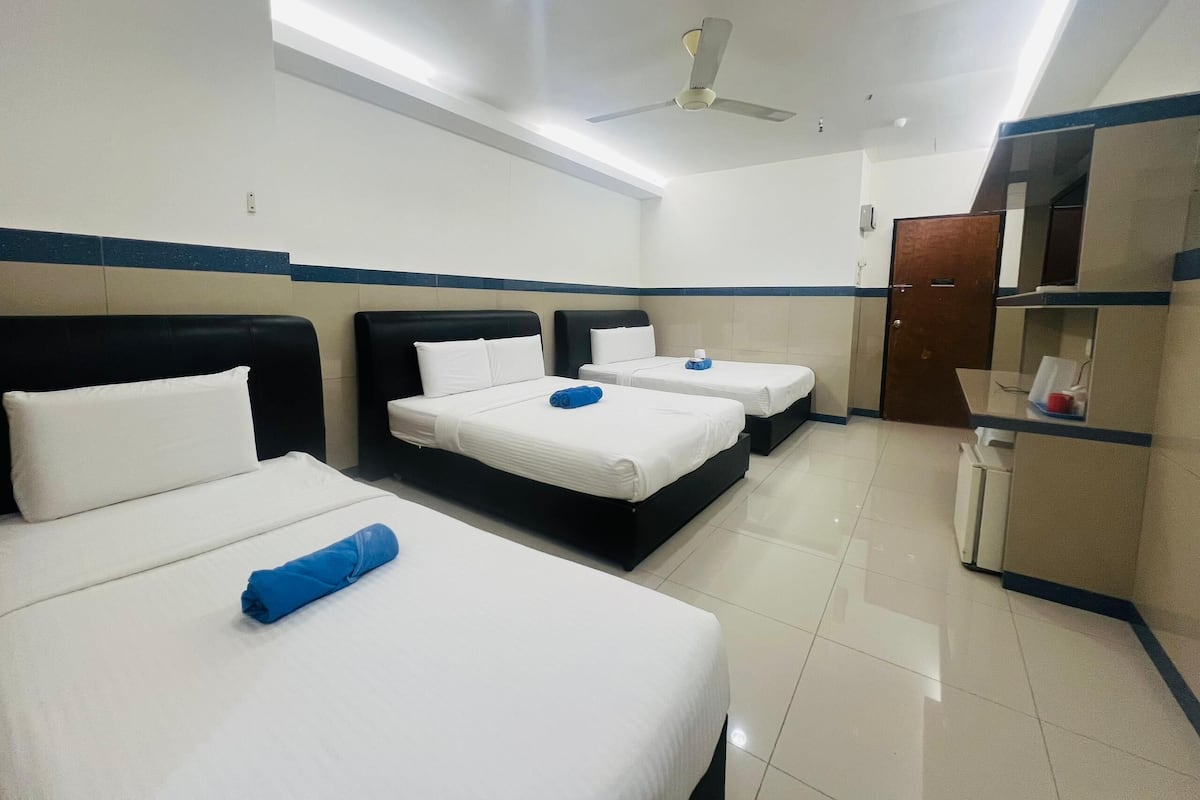 A hotel room with three beds, a ceiling fan, and a minibar.