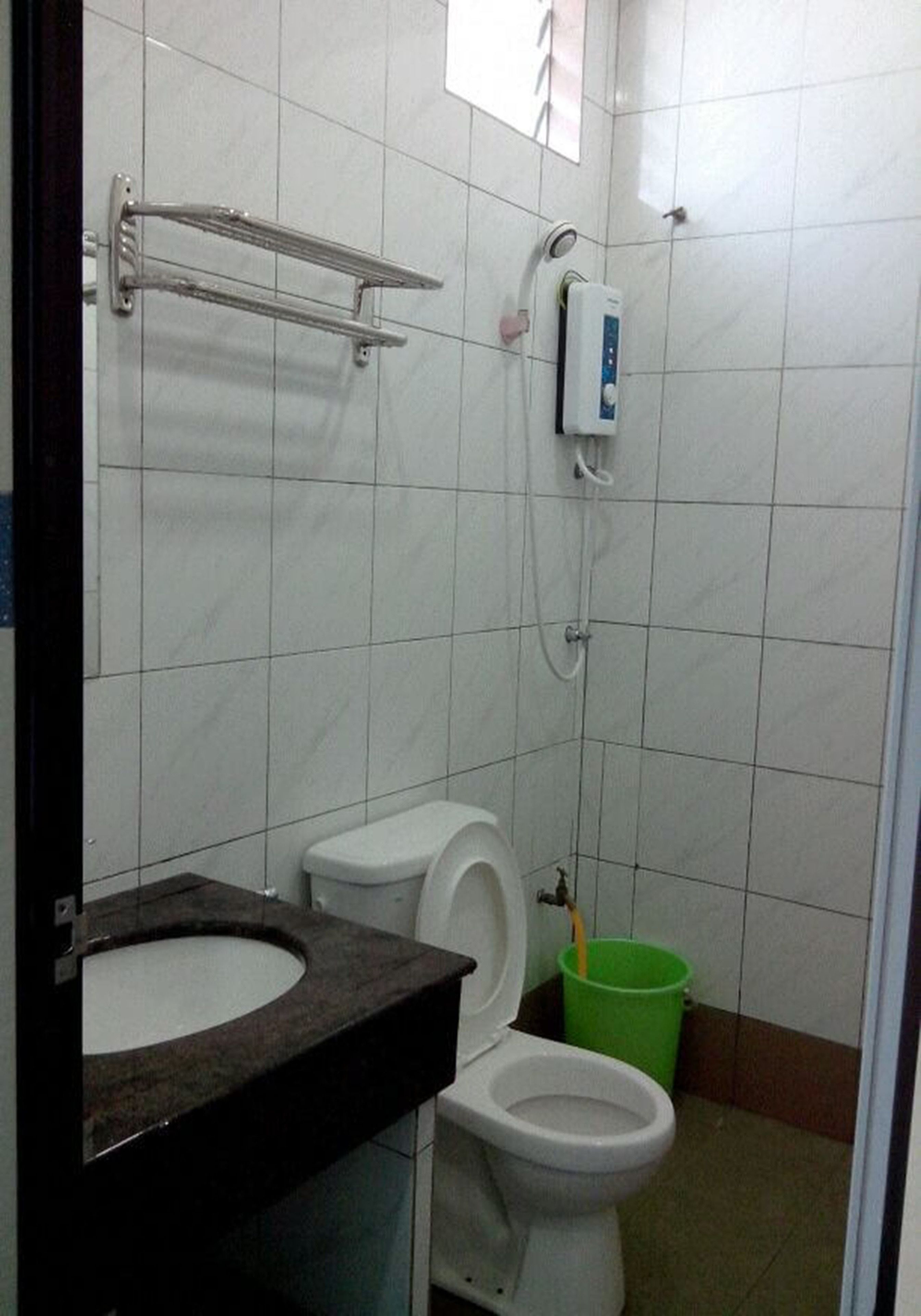 Un baño con inodoro, lavamanos, ducha y un cubo de basura verde.