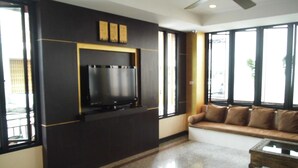 Un salon moderne avec un téléviseur à écran plat fixé à un mur foncé, un canapé avec des coussins et une table basse.