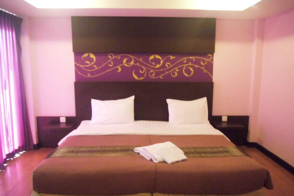 Una habitación de hotel con una cama grande, dos almohadas, un cabecero con diseño decorativo y una mesita de noche con una lámpara.
